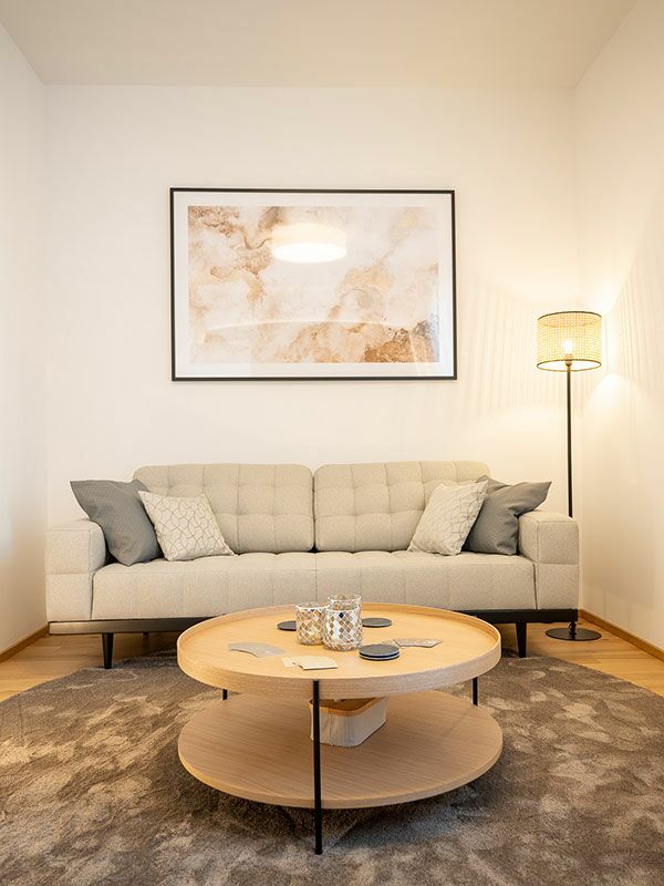 In dem Raum für die psychosoziale Beratung, Supervision und Hypnose steht eine graue Couch, ein Holztisch auf einem Teppich, eine Stehlampe in der Ecke und ein großes Bild hängt an der Wand.